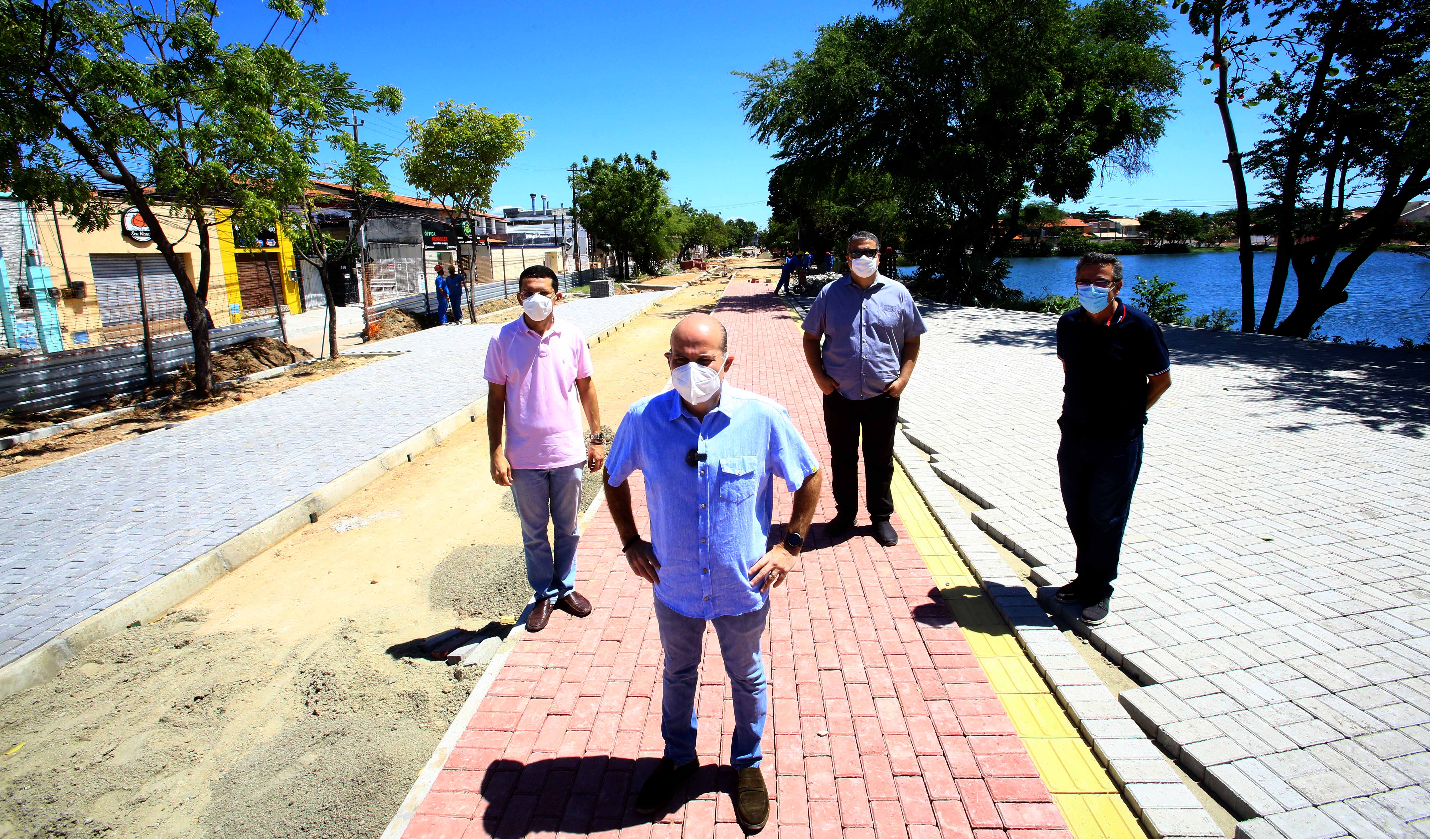 prefeito e três secretários em pé posando para a foto, usando máscara e com lago ao fundo